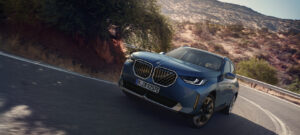 Graublauer BMW X3 fährt auf einer Straße zwischen beeindruckenden Bergen, umgeben von einer atemberaubenden Naturkulisse
