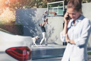 Frau telefoniert neben dem Wagen und Mann, Kind und Hund spielen im Hintergrund.