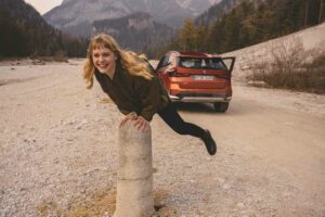 Eine Frau springt auf den Bergen und der BMW X1 steht offen dahinter.