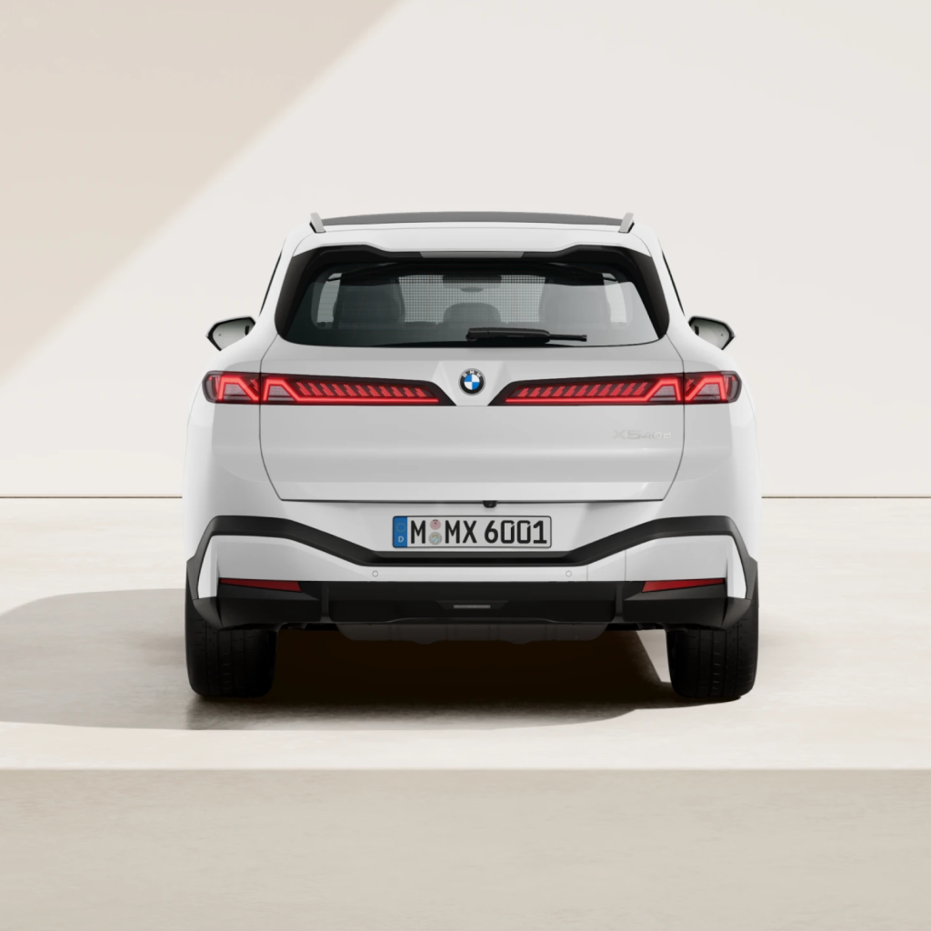 Rückansicht eines weißen BMW-Elektro-SUV, der auf einem hellen Untergrund geparkt ist; zu sehen sind die schlanken Rückleuchten, ein BMW-Emblem und ein europäisches Kennzeichen mit der Aufschrift „M MX 6001“ in der Mitte.